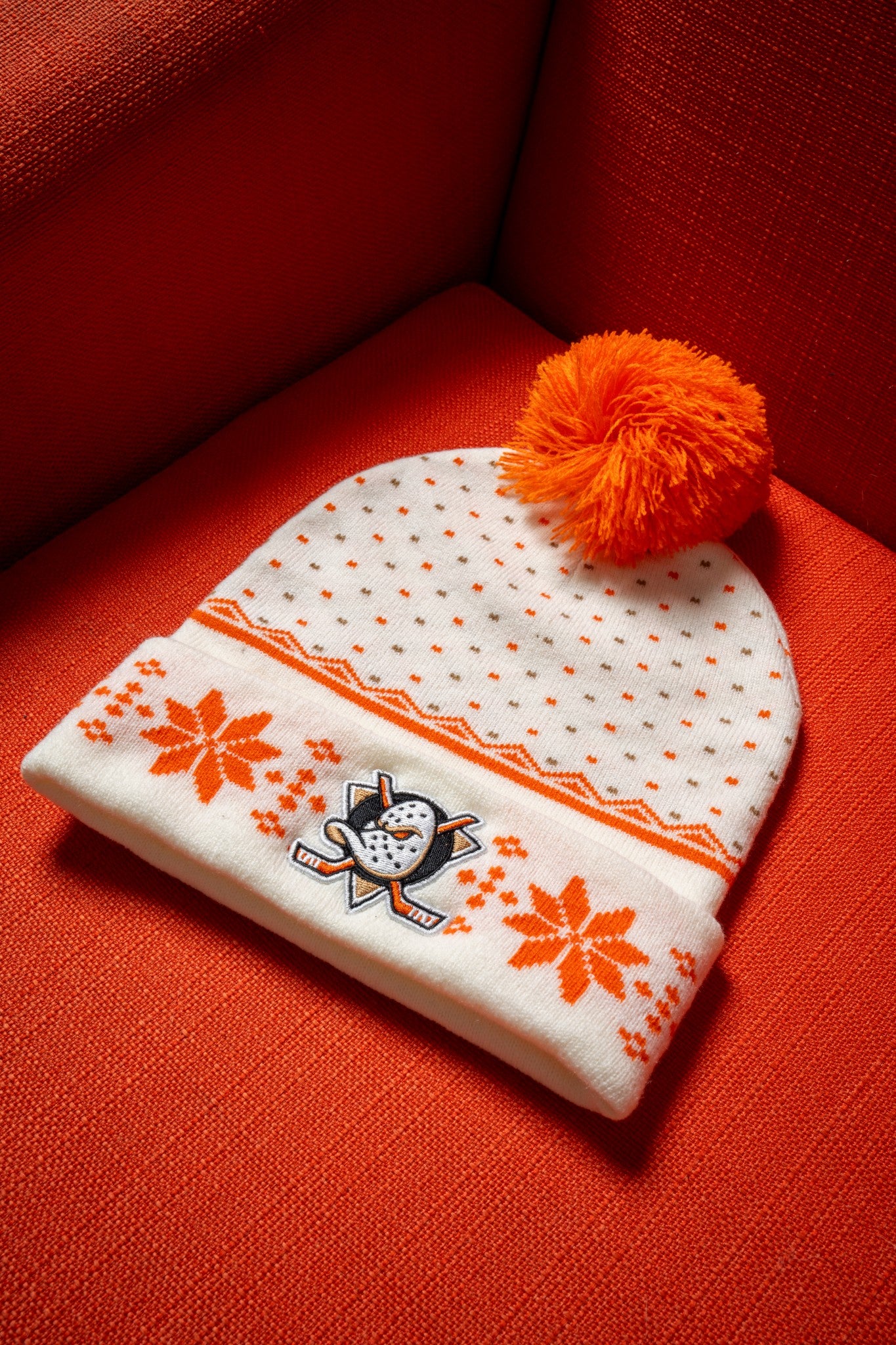 White beanie with orange patterns, Anaheim Ducks logo and orange pom-pom on a bright orange-red chair