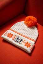 White beanie with orange patterns, Anaheim Ducks logo and orange pom-pom on a bright orange-red chair